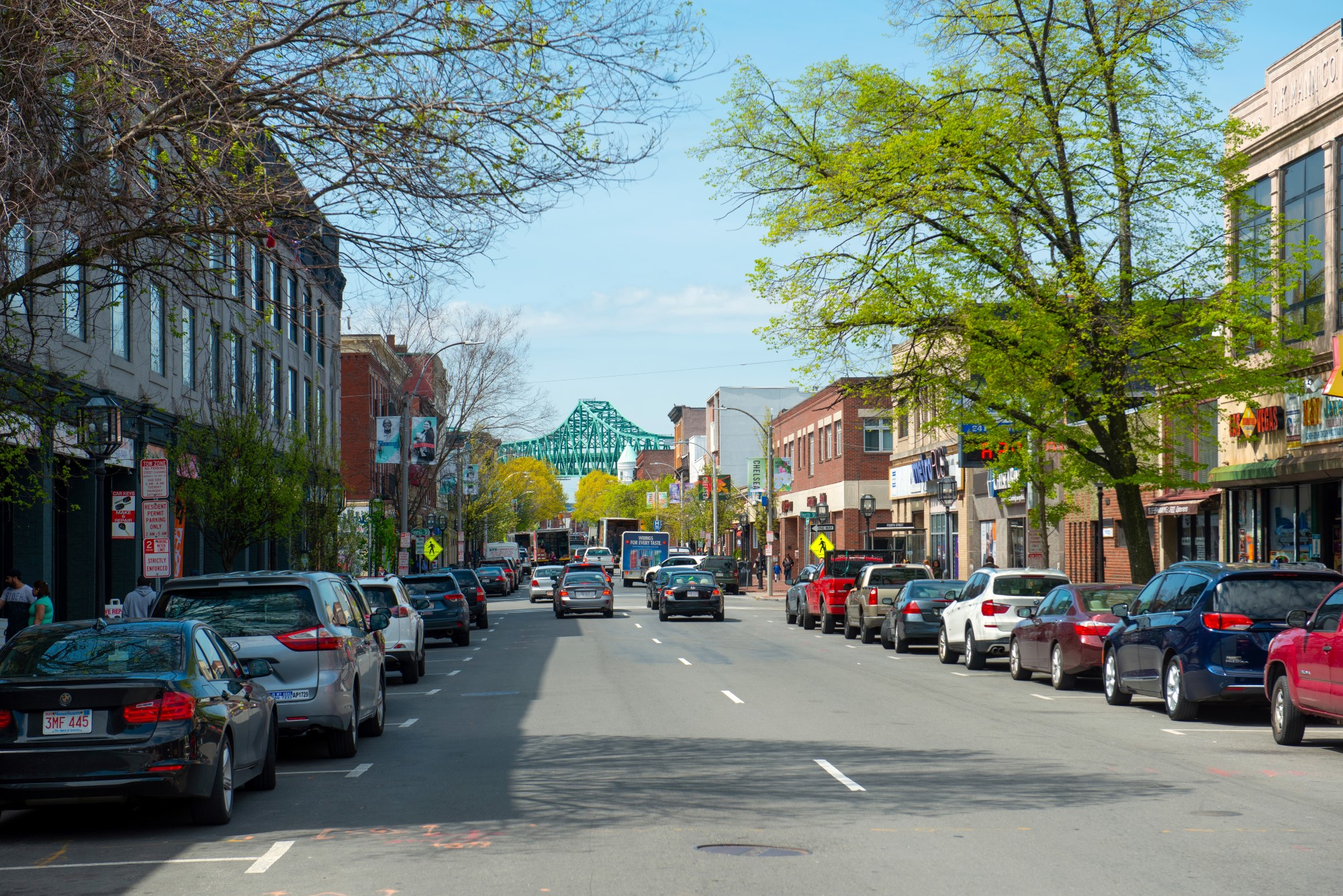 A photograph of a street in downtown Chelsea, Massachusetts. Parallel-parked cars line both sides of the road. In the distance is the Tobin Bridge.